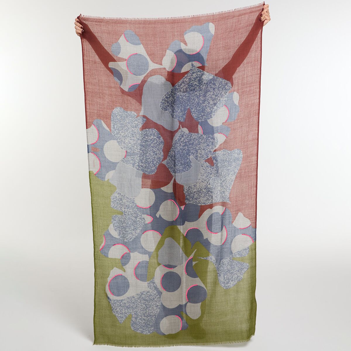 Langer, rechteckiger Wollschal in den Farben Khaki und Rose mit floralem Muster und feiner Stickerei. Der Schal wird im Hochformat gehalten und zeigt verschiedene abstrakte Blütenformen in hellen Blau-, Grau- und Weißtönen. Das untere Drittel ist khaki, der obere Bereich roséfarben. Der Schal wirkt leicht und luftig. Geeignet als modisches Accessoire für modebewusste Frauen.
