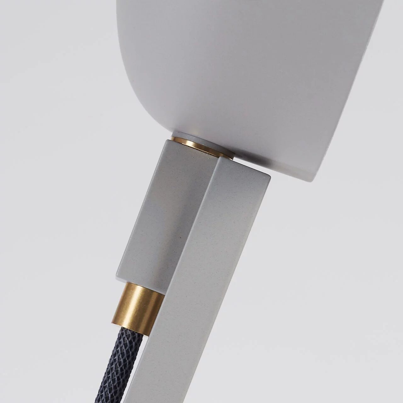 Detailaufnahme des oberen Teils der Stehleuchte »schliephacke« von mawa design in Grau: runder Leuchtenkopf aus matt grauem Aluminium, geradliniges Gestell, sichtbares Textilkabel in Schwarz mit messingfarbenem Übergang, minimalistisches, modernes Design.