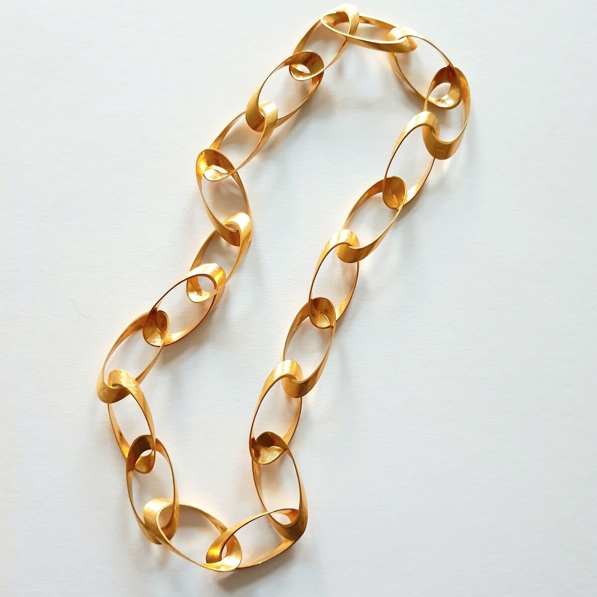 Dieses Bild zeigt ein elegantes, goldenes Collier mit ovalen Gliedern, das auf einer weißen Oberfläche liegt. Es betont Luxus und Stil.