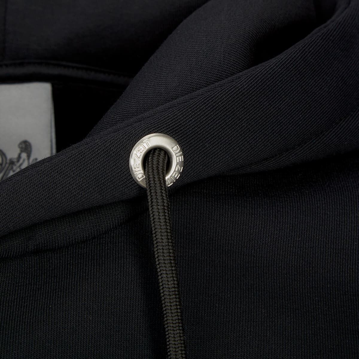 Nahaufnahme eines schwarzen Hoodies der 'ZEIT-Kollektion' mit silbernen 'DIE ZEIT' Details an der Kordel.