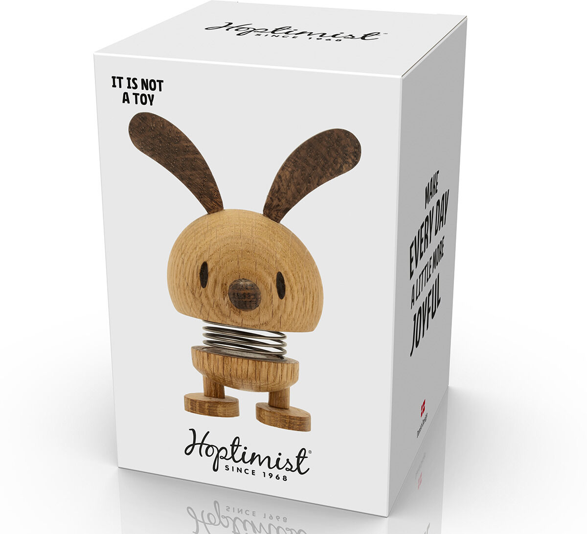 Eine Hoptimist-Bunny-Figur aus Eiche, dargestellt auf einem Karton mit der Aufschrift 'It is not a toy'. Die Figur hat große Ohren und eine Spiralfeder als Unterkörper. Perfekte Dekoration für Ostern und andere Anlässe.
