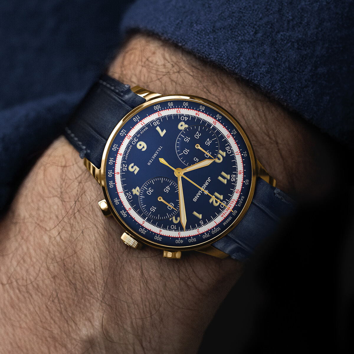 Eine goldfarbene Armbanduhr der ZEIT-Sonderedition »Telemeter« mit blauem Lederarmband und blauem Zifferblatt, getragen am Handgelenk einer Person im blauen Ärmel. Die Uhr besitzt einen Chronographen und präzise Skalen, umgeben von einem eleganten Design.