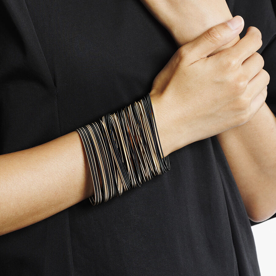 Person trägt ein elegantes Armband in Bronze und Schwarz an ihrem Handgelenk. Der Schmuck besteht aus mehreren feinen Strängen und ergänzt einen stilvollen, modischen Look.