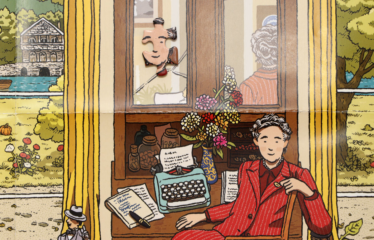 Illustration eines Puzzles mit Bezug zu Agatha Christie. Ein Raum mit einer Person in einem roten Anzug, die an einem Schreibtisch sitzt. Auf dem Schreibtisch befinden sich eine Schreibmaschine, Bücher und Blumen. Im Hintergrund ein Fenster mit Blick auf eine Naturkulisse und Figuren im Garten. Die Farben sind überwiegend Rot, Blau, Grün, Gelb, Braun und Beige.