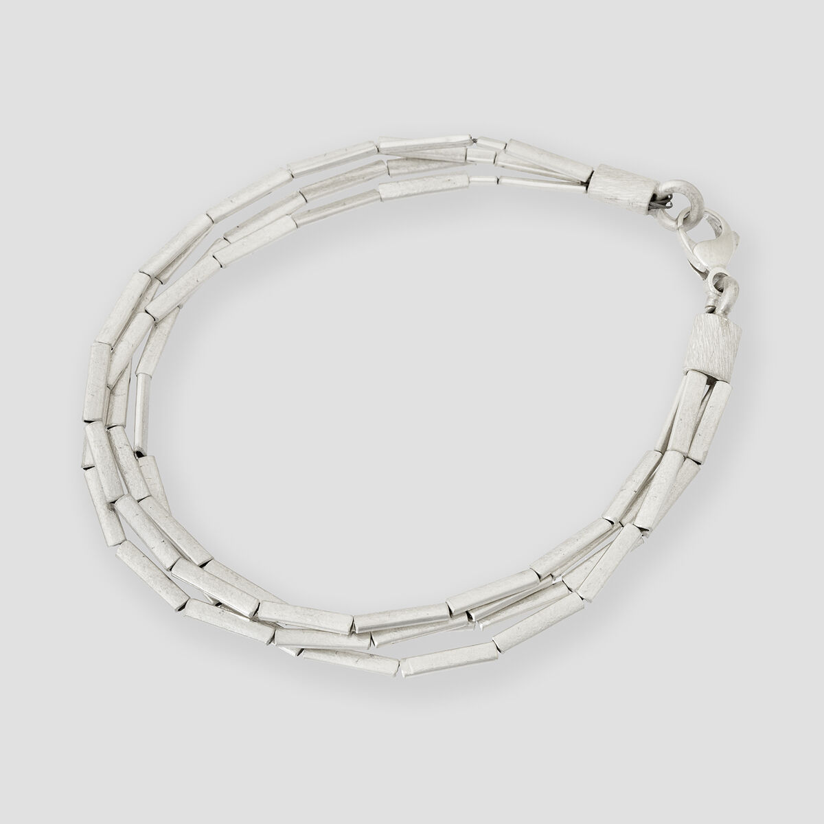 Abgebildet ist ein feines Halmarmband aus glänzendem Silber mit schlichten, röhrenförmigen Gliedern und einem Verschluss, liegend vor einem hellgrauen, neutralen Hintergrund.