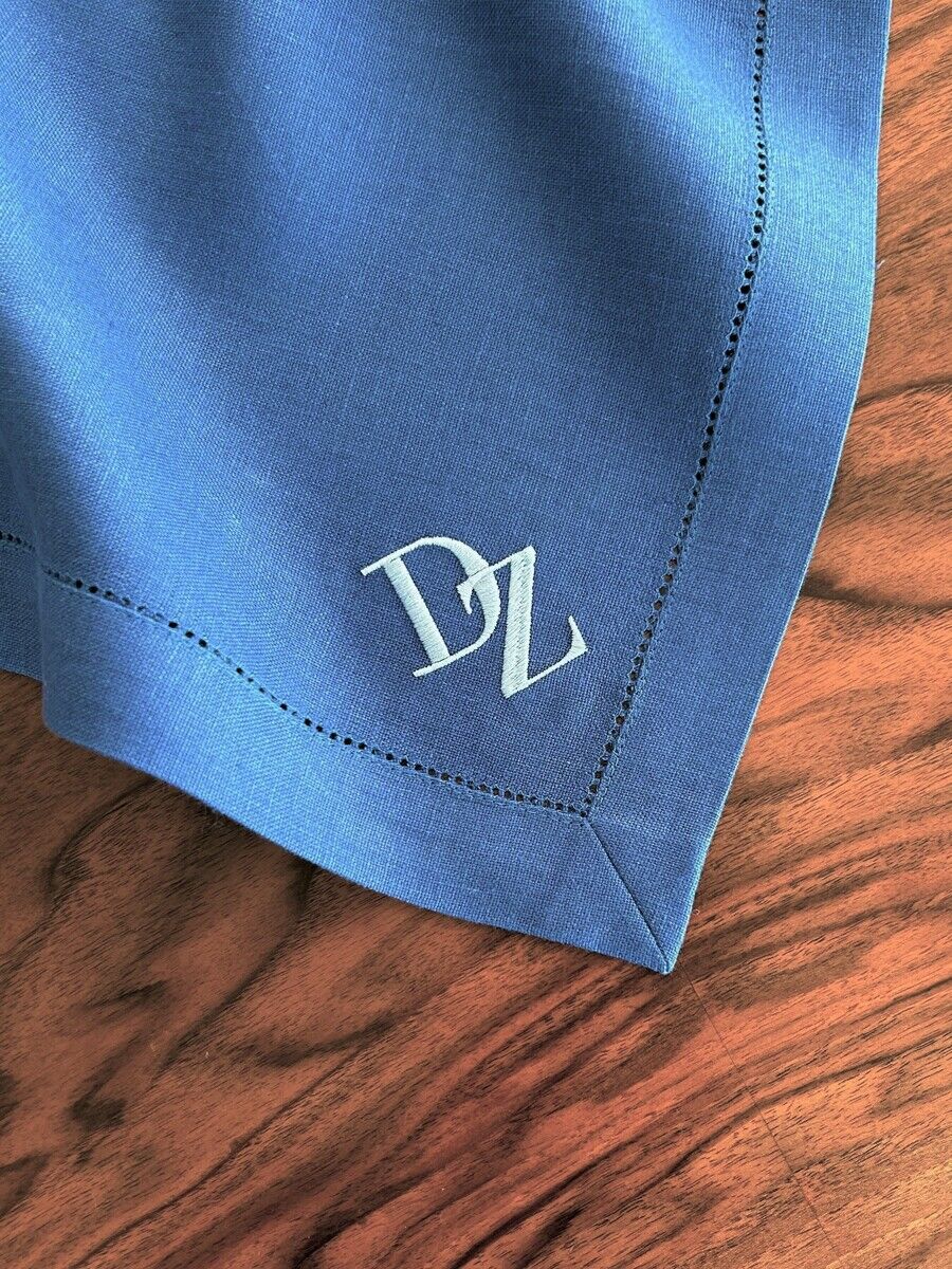 Blaues Leinen-Serviette mit einem weißen Monogramm 'D Z' in der Ecke, auf einem Holztisch drapiert.