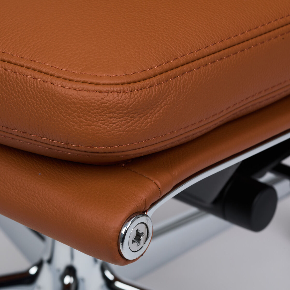 Detailaufnahme einer Sitzfläche aus cognacfarbenem Leder des ZEIT-Sonderedition Schreibtischstuhls »Vitra Soft Pad EA219«. Hochwertige Polsterung mit markanter Naht, elegant abgerundete Kanten und verchromte Verschraubungen auf glänzendem Untergestell.