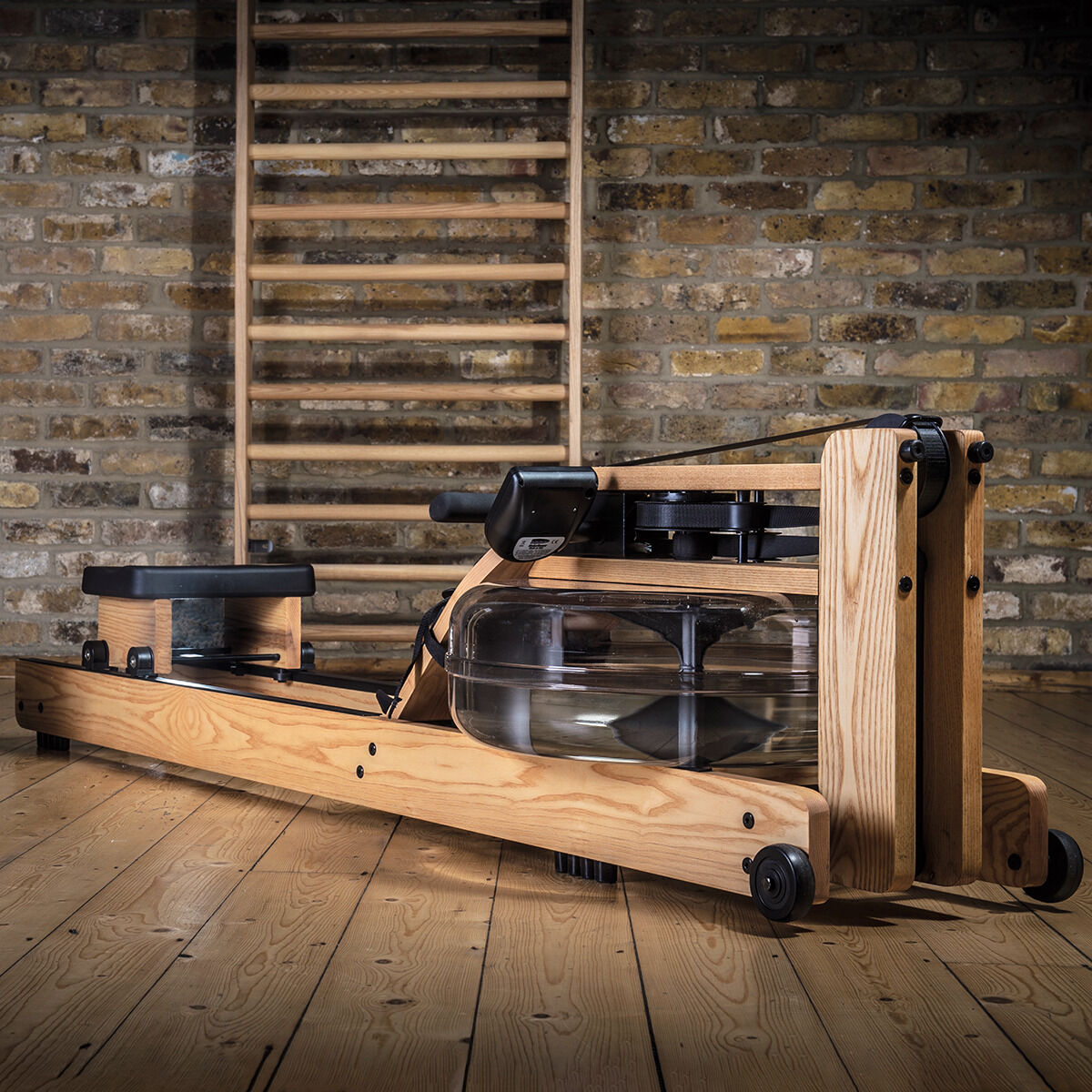 Ein Waterrower-Rudergerät aus Eiche auf einem Holzboden vor einer Ziegelwand, geeignet für Heimtraining.