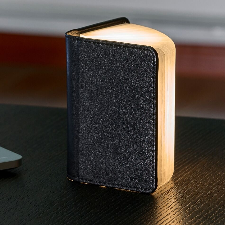 Ein Smart Booklight aus schwarzem Leder in Buchform, das auf einem Tisch steht und warm weißes Licht ausstrahlt. Es wirkt modern und elegant, ideal als dekorative Beleuchtung in Wohn- oder Schlafzimmer.