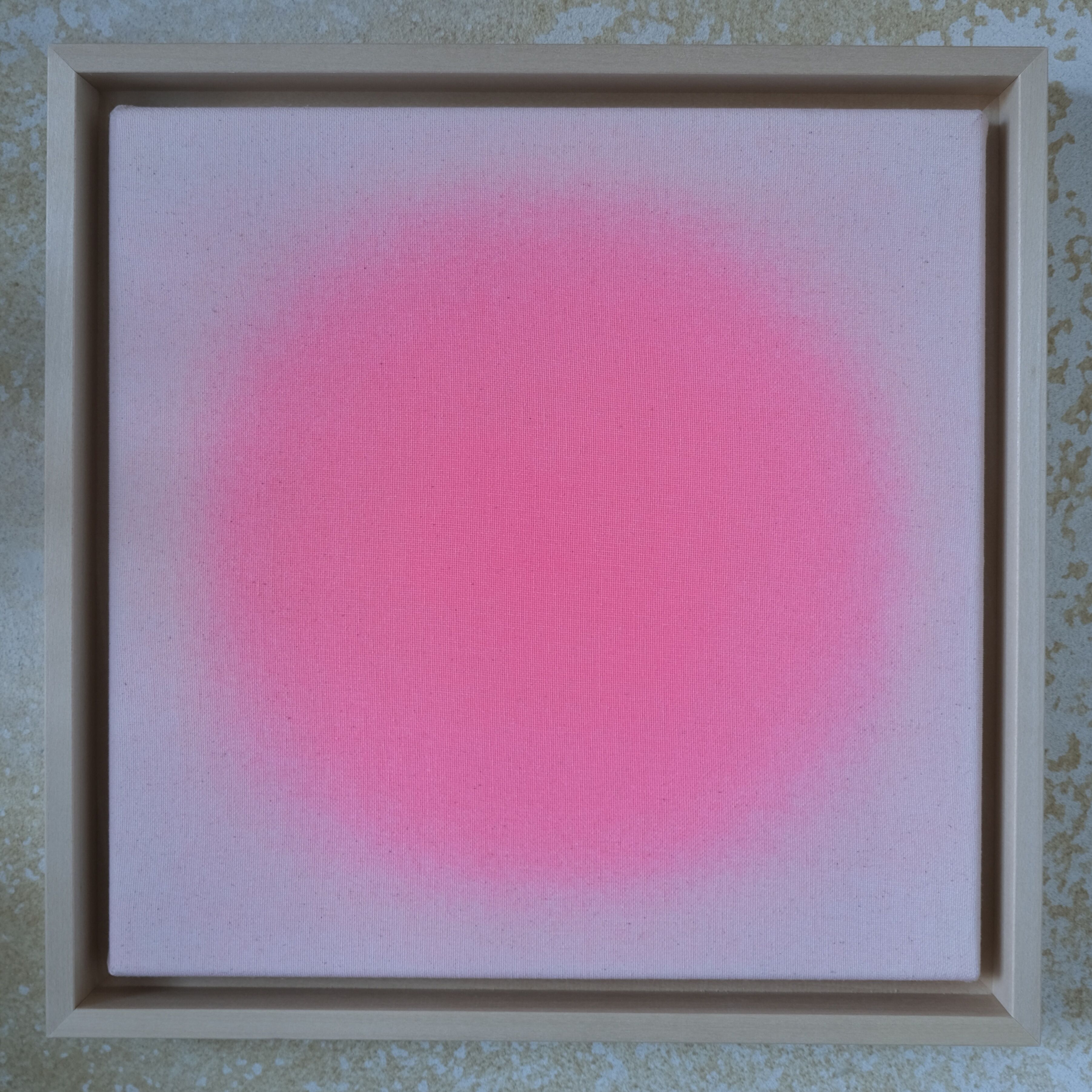 Quadratisches Kunstwerk mit zartem Apricot-Pink, das in der Bildmitte kräftig leuchtet und sanft nach außen verläuft. Sichtbare Textur auf naturbelassener Leinwand, eingefasst in einen hellen Lindenholzrahmen. Im Hintergrund eine helle, grob strukturierte Fläche.