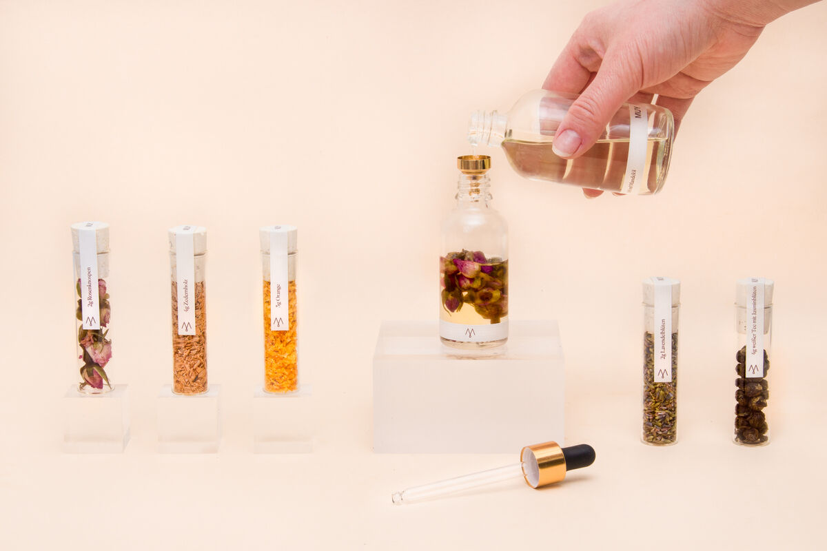 Naturkosmetik-Set »MUY« mit verschiedenen Fläschchen und Reagenzgläsern, gefüllt mit natürlichen Inhaltsstoffen und ätherischen Ölen. Eine Hand gießt Flüssigkeit in ein Glasfläschchen. Das Set bietet eine luxuriöse Pflege mit nachhaltigen und veganen Produkten.