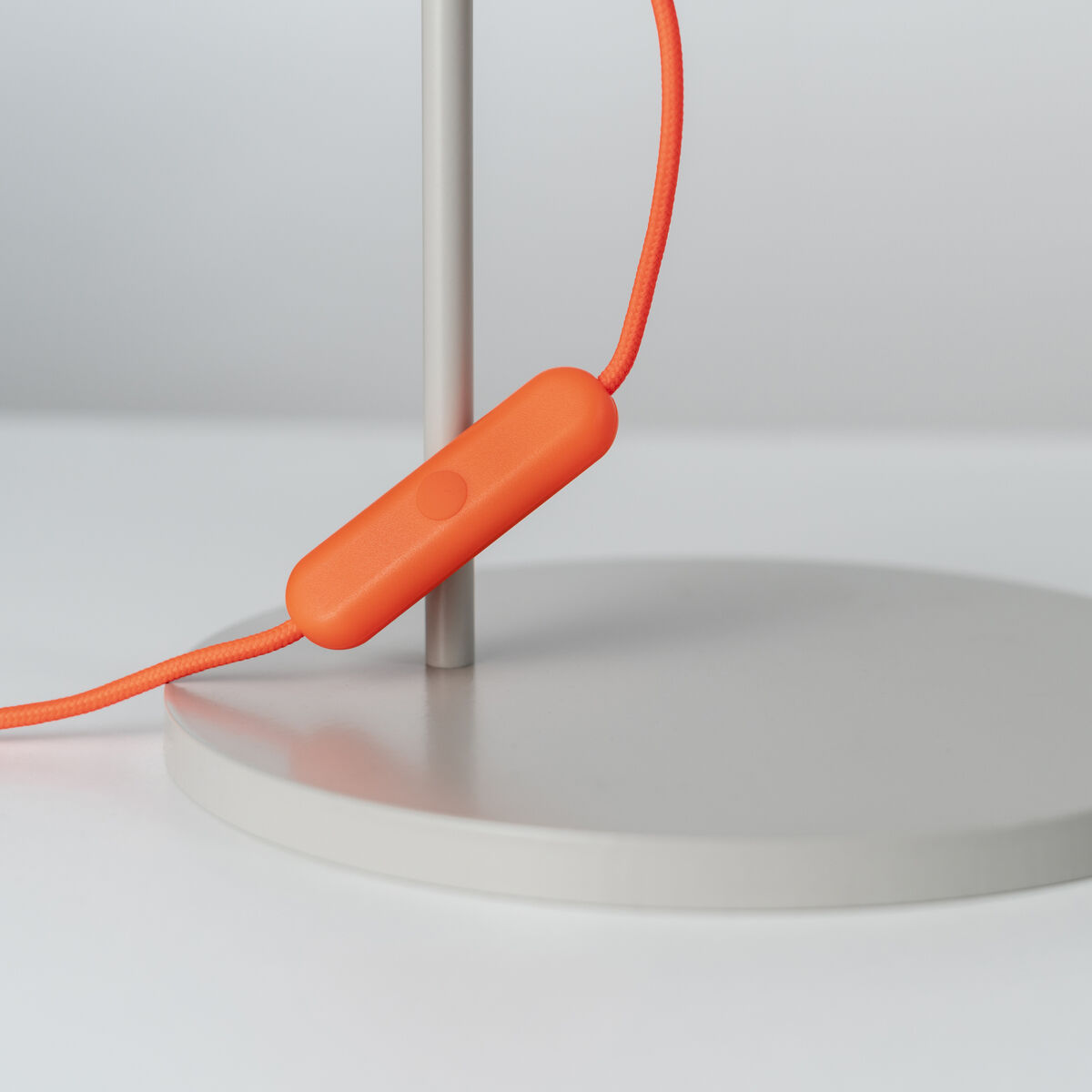 Eine moderne Tischlampe mit grauem Fuß und orangefarbenem Kabel. Die Lampe hat ein minimalistisches Design und eignet sich gut für zeitgenössische Einrichtungen.