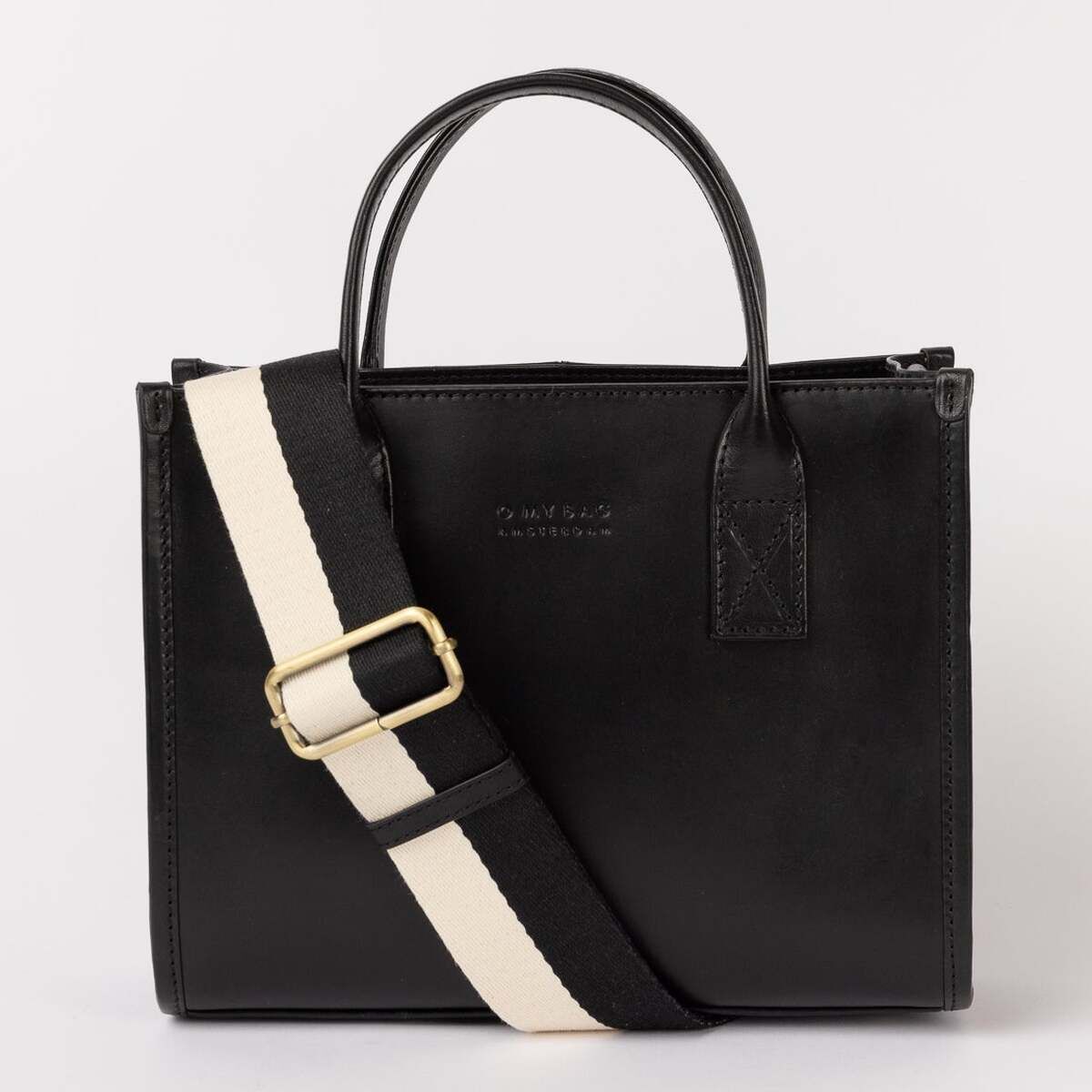 Schwarze Ledertasche mit kurzem Henkel und einem abnehmbaren cremeweißen Schulterriemen mit goldener Schnalle, stehend vor neutralem Hintergrund.