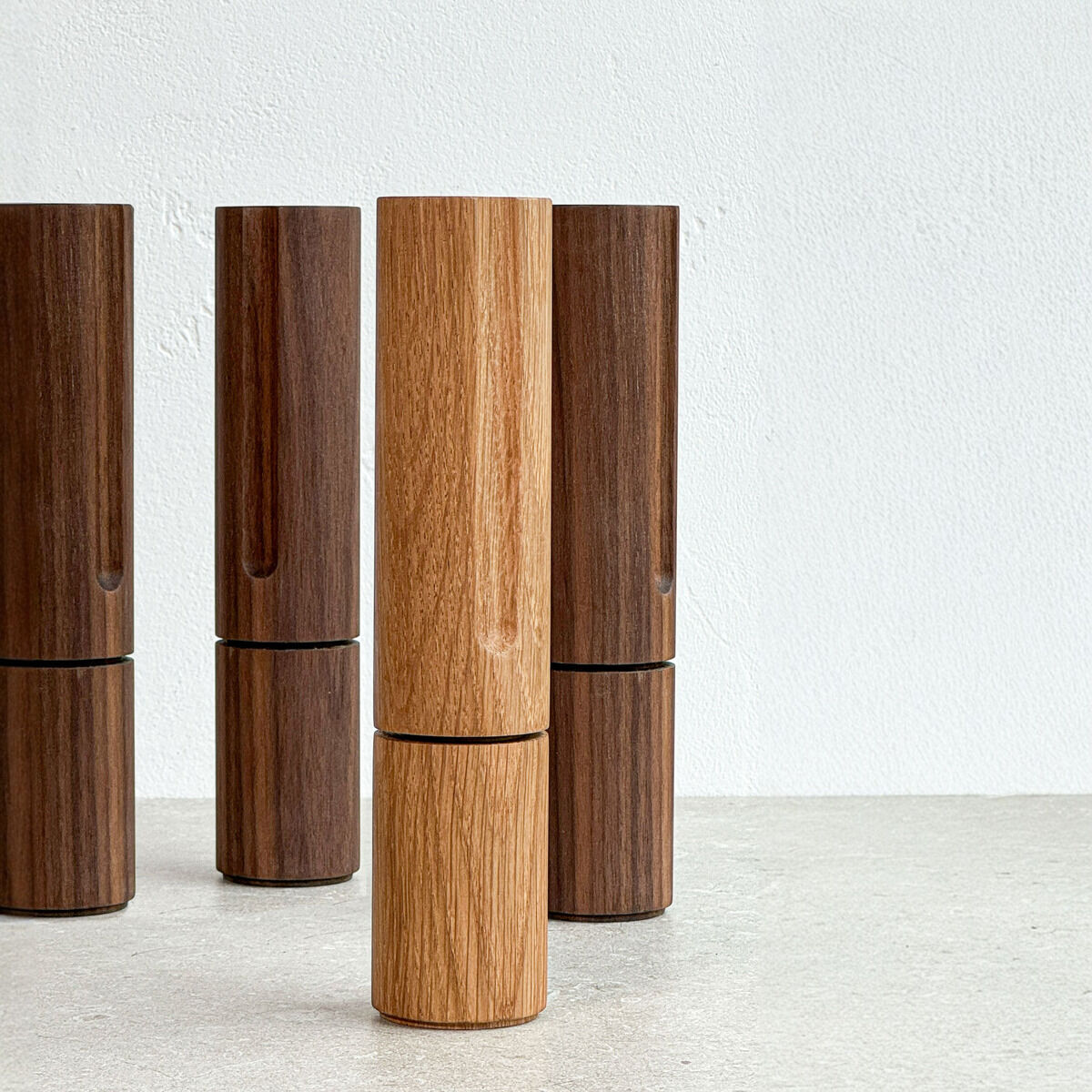 Vier Gewürzmühlen aus Holz, Modell »TURN« der Marke finbeaux, gestaltet von Christoph Schoen. Vordergrund helles Holz (Walnut-Variante), Hintergrund drei dunkle Mühlen. Alle stehen auf heller Steinoberfläche vor weißer Wand, zylindrisches und minimalistisches Design.