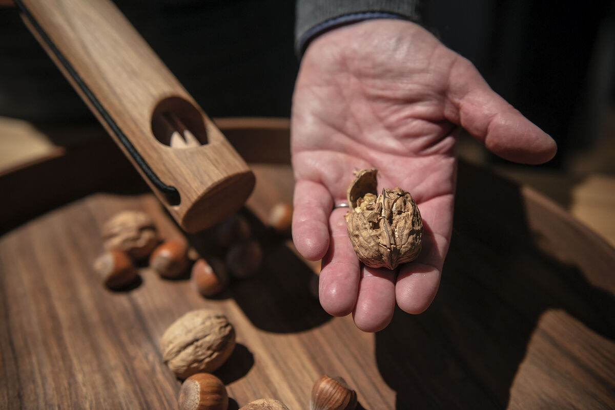 Holz-Nussknacker im Einsatz: Eine Hand hält eine geknackte Walnuss über einer Holzschale mit weiteren Nüssen, während der Nussknacker daneben liegt.