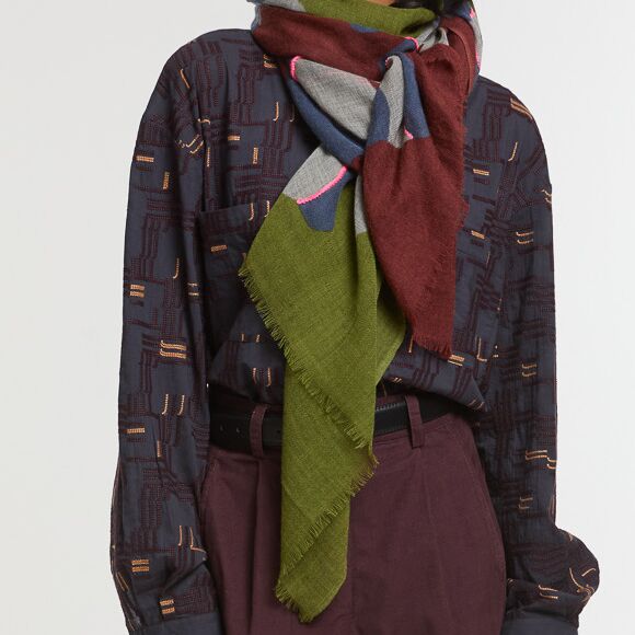 Das Bild zeigt einen modischen Wollschal »Eternel« mit Stickerei in den Farben Khaki und Rosa, kunstvoll um den Hals einer Person drapiert. Der Schal besteht aus mehreren Farbflächen, darunter Khaki und dezentes Rosa, und eignet sich als modernes Accessoire für Herbst und Winter.