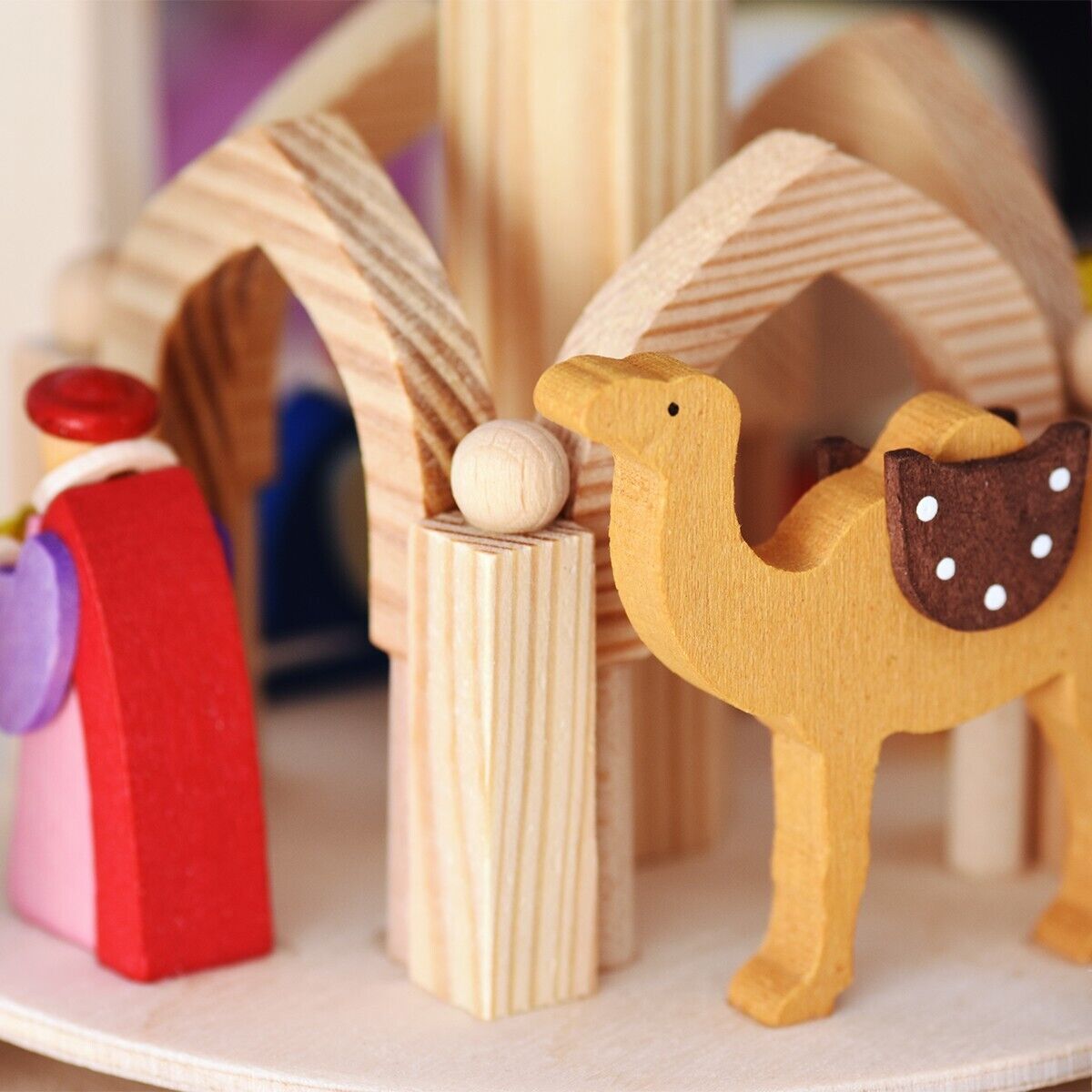 Holzpyramide mit der Darstellung der Geburt Christi, einschließlich Teelicht- und Pyramidenkerzenhalter. Eine geschnitzte Figur eines roten, braunen und violetten Kamels ist prominent sichtbar. Die Pyramide hat eine einfache Holzoptik und ist für die Weihnachtsdekoration geeignet.