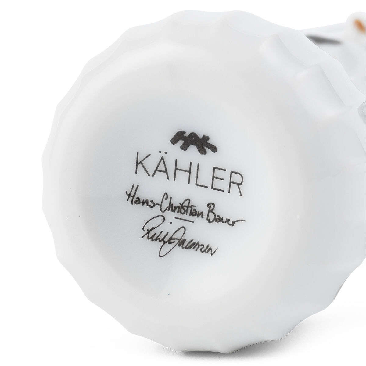 Die Unterseite eines schlichten, weißen Porzellan-Anhängers in Form eines Schneemädchens von Kähler ist zu sehen. Auf dem Boden ist das Kähler-Logo sowie der Name des Designers aufgedruckt.