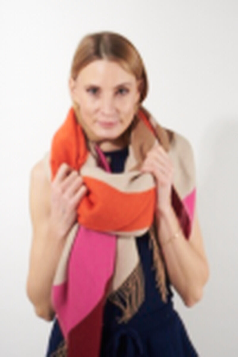 Eine Frau trägt einen Cape »Lucma« aus Alpaka-Wolle in den Farben Orange, Beige und Pink. Der Cape ist weich und kuschelig und eignet sich ideal für die kalte Jahreszeit.