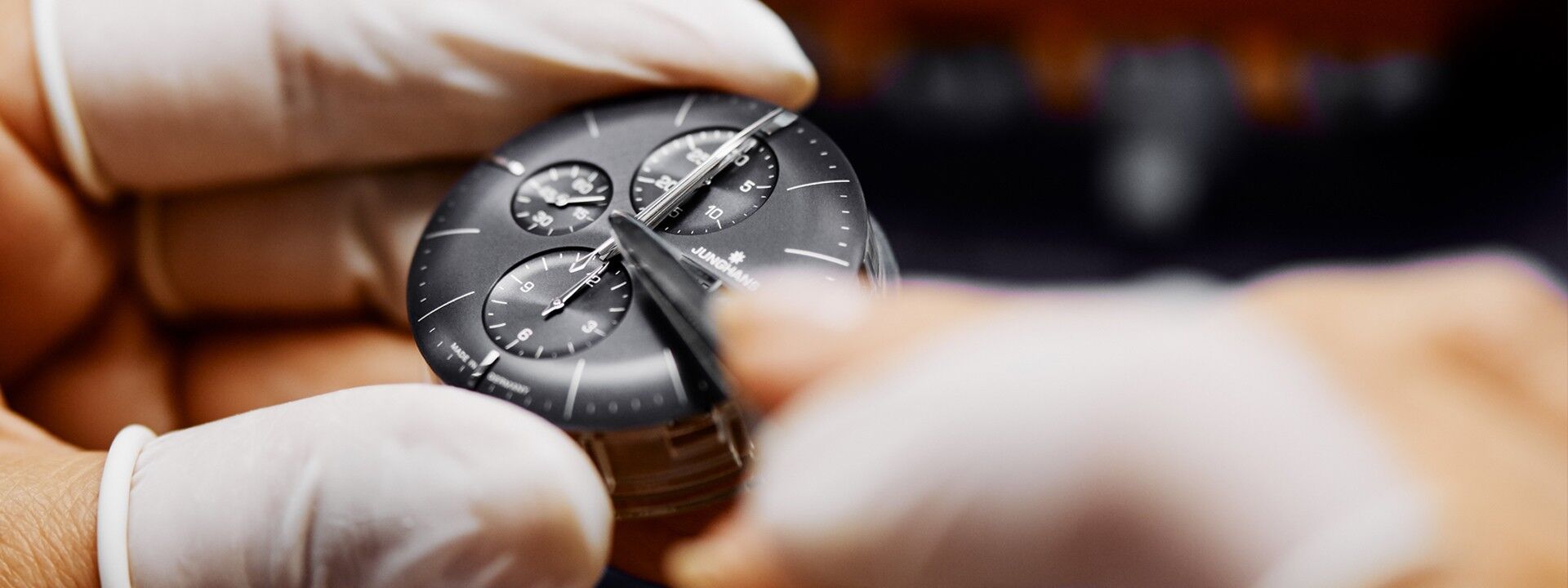 Nahaufnahme einer Uhr, die mit einem Werkzeug sorgfältig justiert wird und deren detailliertes schwarzes Zifferblatt und mehrere Zifferblätter zur Geltung kommen.