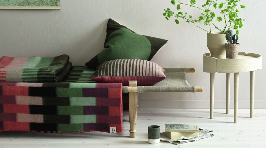 Bunte gestrickte Decken und Kissen auf einer Holzbank neben einem kleinen runden Beistelltisch mit Pflanzen