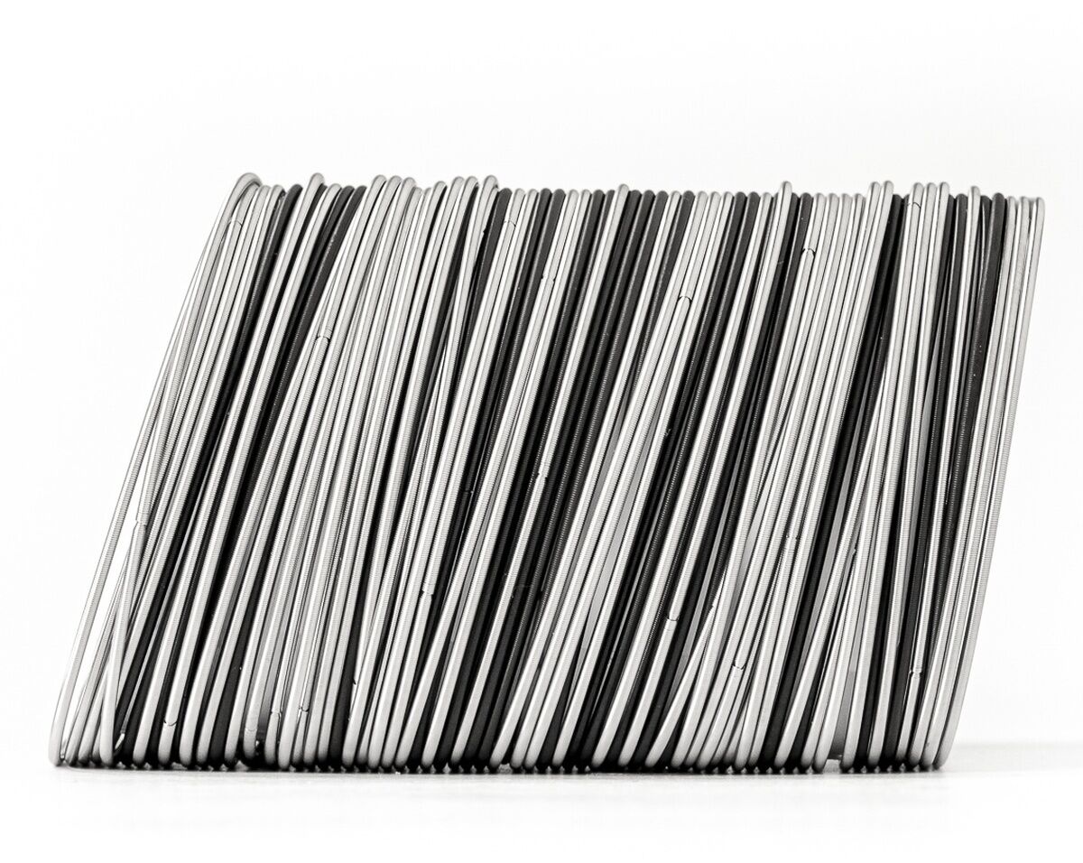 Abgebildet ist ein breites, modernes Armband aus bronze- und silberfarbenen Metallstreifen, die dicht nebeneinander in dynamischer Anordnung stehen. Das Schmuckstück wirkt minimalistisch und kunstvoll und eignet sich als stilvolles Accessoire für verschiedene Anlässe.