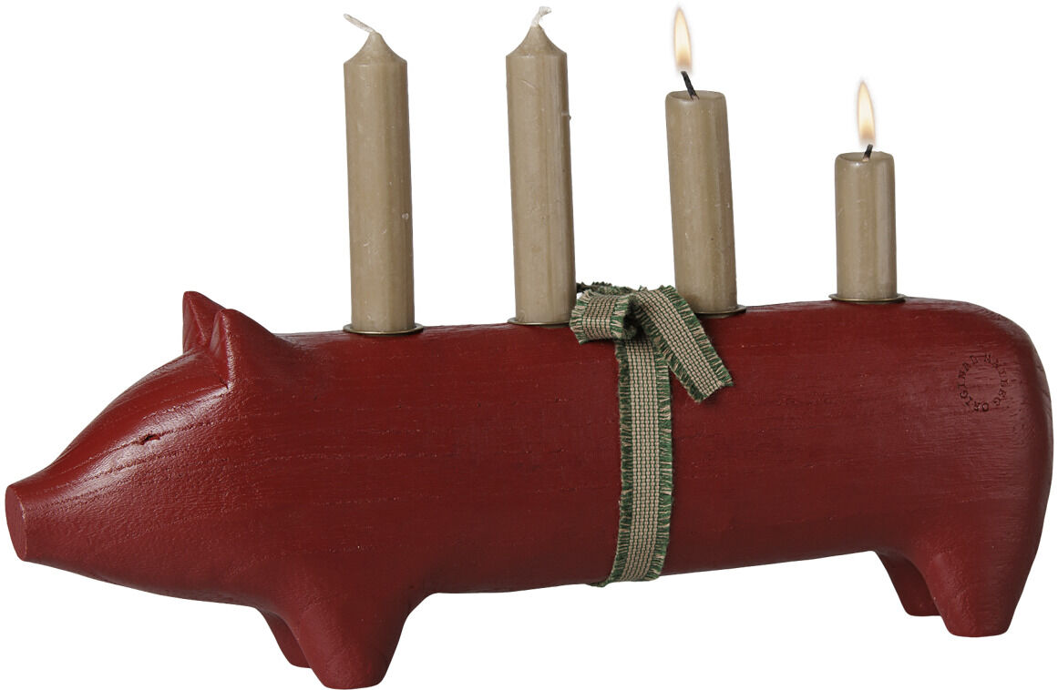 Großer Kerzenhalter in Form eines roten Holz-Schweins der Marke Maileg. Vier beige Kerzen stehen in einer Reihe auf dem Rücken, einige brennen. Ein grünes Schleifenband ist um den Körper gebunden. Das Schwein steht auf vier Beinen vor weißem Hintergrund.