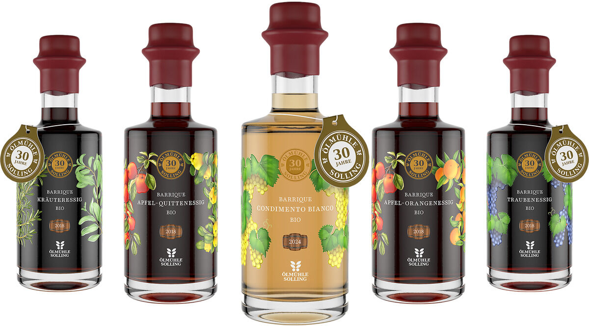 Fünf hochwertige Essigflaschen in einer Reihe, jeweils mit dunklen roten Verschlüssen und Jubiläumsetikett, dekorativ gestaltet mit verschiedenen Frucht- und Kräutermotiven auf schwarzem oder hellem Hintergrund, Markenlogo Ölmühle Solling sichtbar.