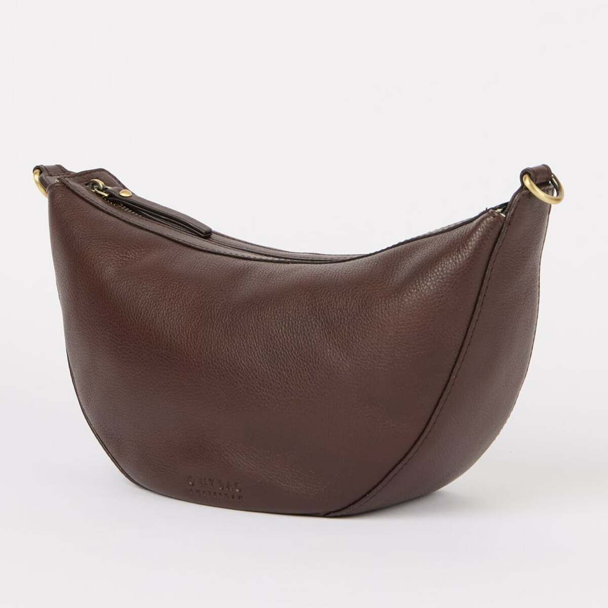Eine mittelgroße Umhängetasche in dunklem Braun mit gebogener Form, aus Lederoptik-Material, mit dezentem goldfarbenem Metall-Detail am Träger, vor hellem Hintergrund.