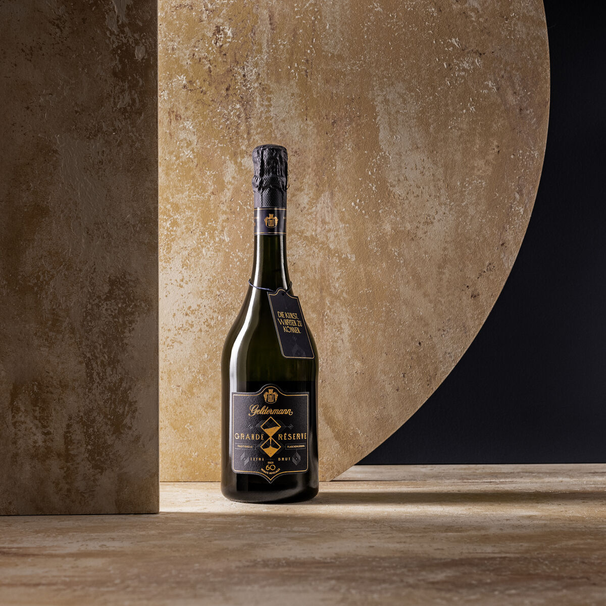 Flasche Geldermann Grande Réserve Sekt auf einem rustikalen Hintergrund mit einem goldenen, halbkreisförmigen Element im Hintergrund. Die Flasche hat ein elegantes, dunkles Etikett.