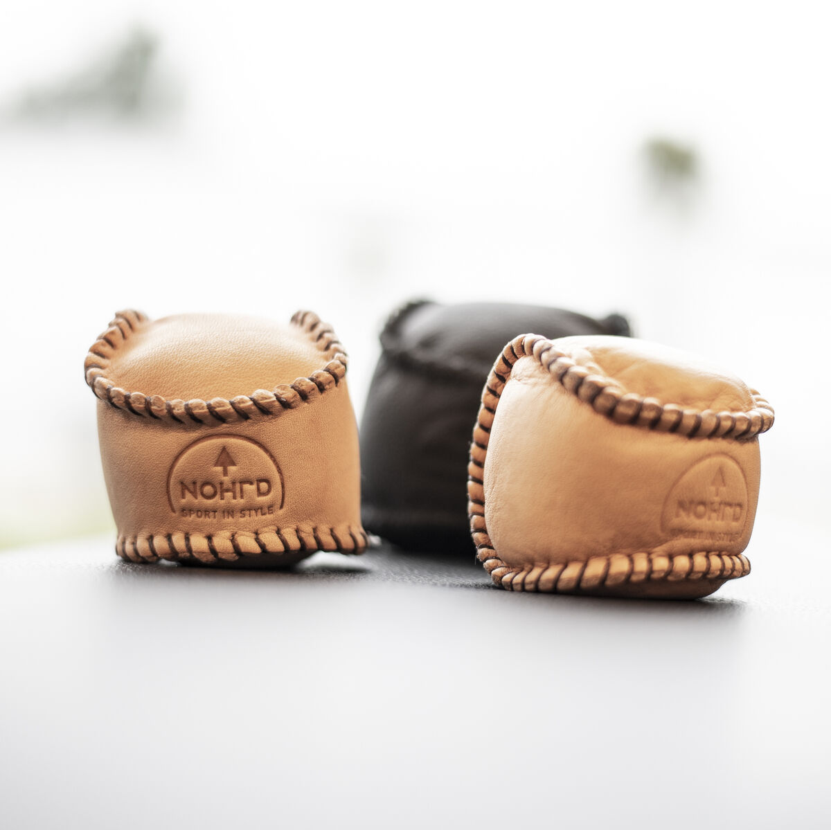 Drei HaptikBälle der Marke NOHrD in natürlichen Farbnuancen Beige und Schwarz, die auf einer Oberfläche platziert sind. Die Bälle sind handgefertigt und für Handtherapie und Stressabbau konzipiert.