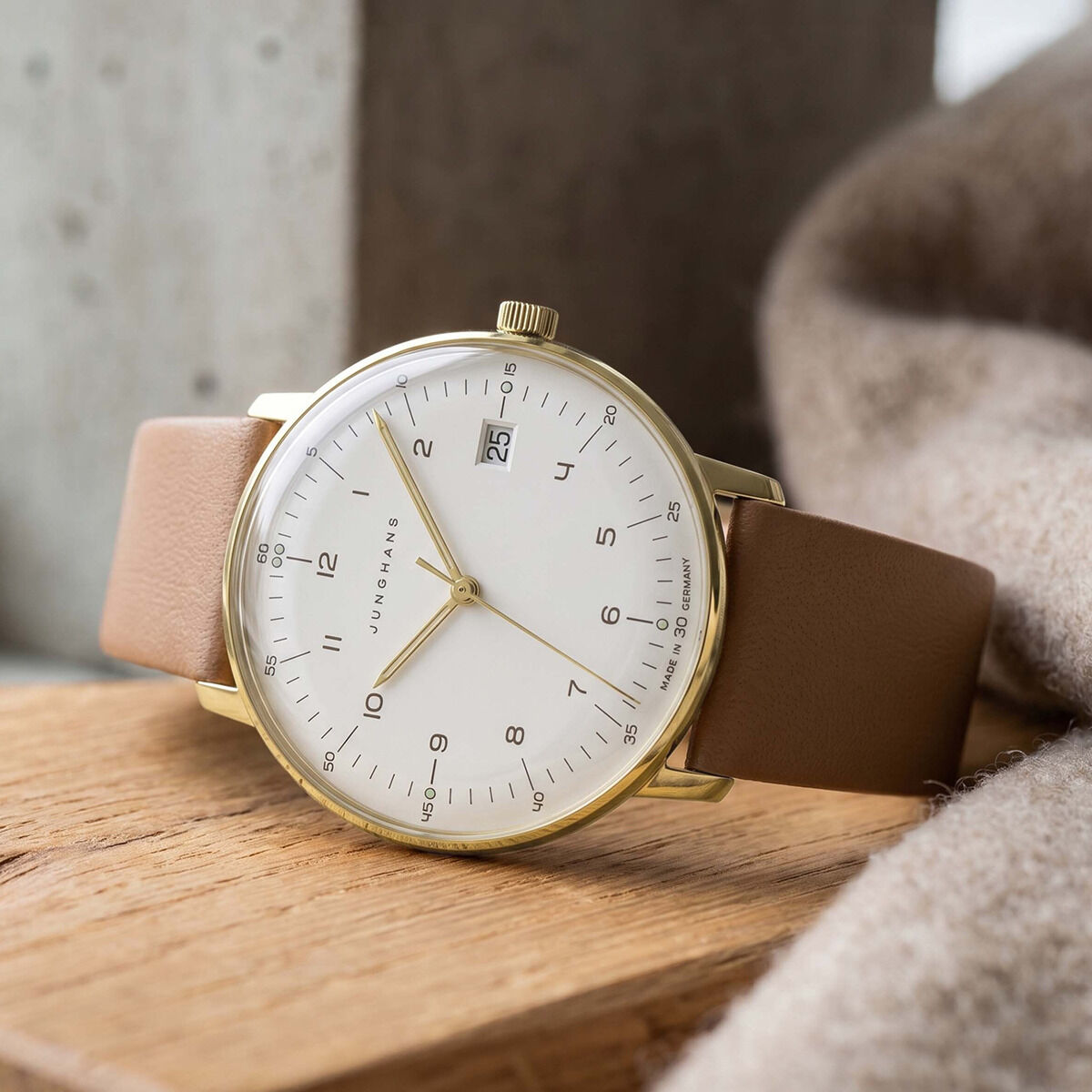 ZEIT-Sonderedition »max bill Damen« Uhr von Junghans mit hellbraunem Lederarmband und weißem Zifferblatt, minimalistisch gestaltete Zahlen, sandgold-mattiertes Edelstahlgehäuse, Datumsanzeige, elegant auf hölzernem Untergrund arrangiert, warme Lichtstimmung.