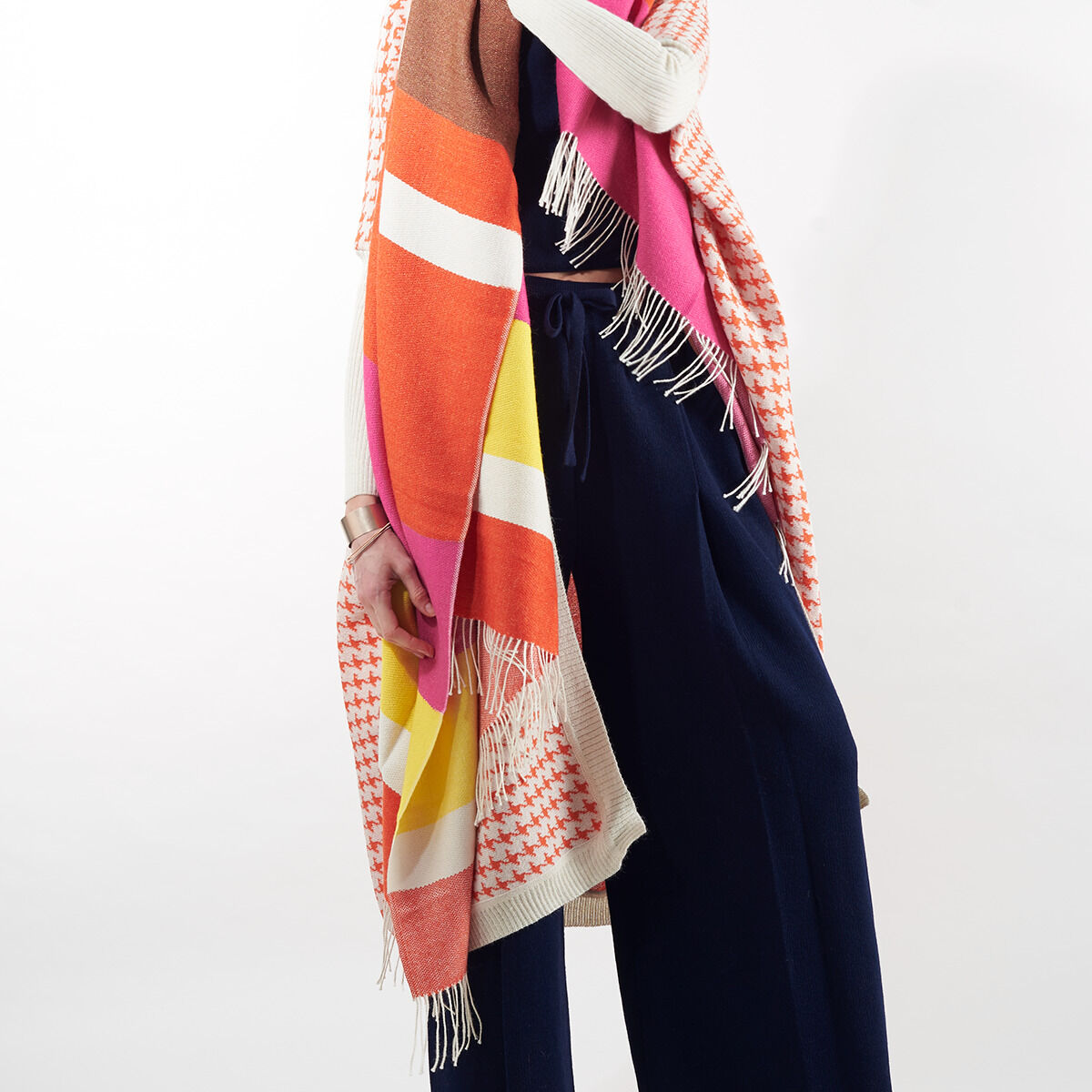 Person trägt das vielfarbige Cape »Surya« aus der ZEIT-Jubiläumsedition. Das Cape zeigt verschiedene Farben wie Pink, Orange, Weiß, Gelb und Blau, wodurch es sehr auffällig und modisch ist. Die Person hat das Cape um ihre Schultern gewickelt.