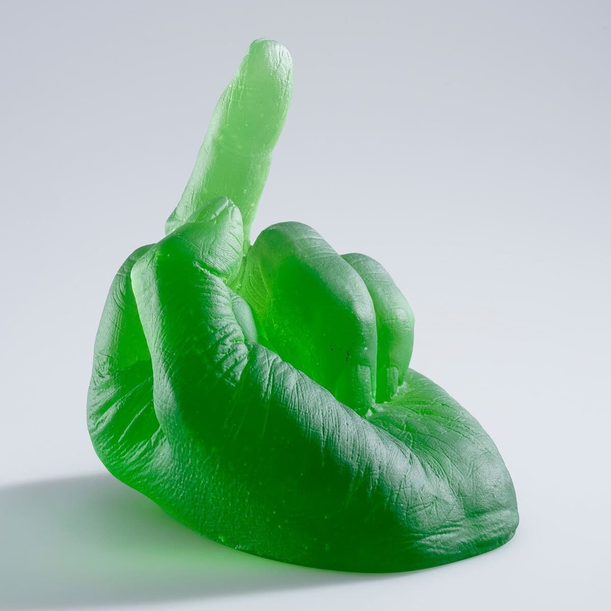 Die Skulptur 'Study of Perspective in Glass' von Ai Weiwei zeigt eine grüne, glasartige Hand, die den Mittelfinger zeigt. Das Kunstwerk steht auf einer glatten, hellen Oberfläche.