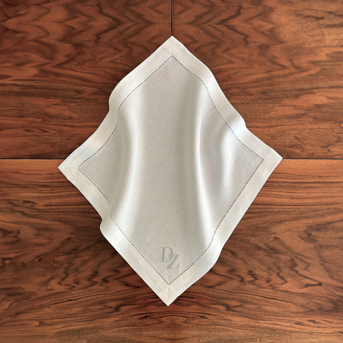 Serviette aus Leinen in Weiß mit Monogramm auf einer braunen Holzoberfläche, sorgfältig gefaltet und elegant präsentiert.