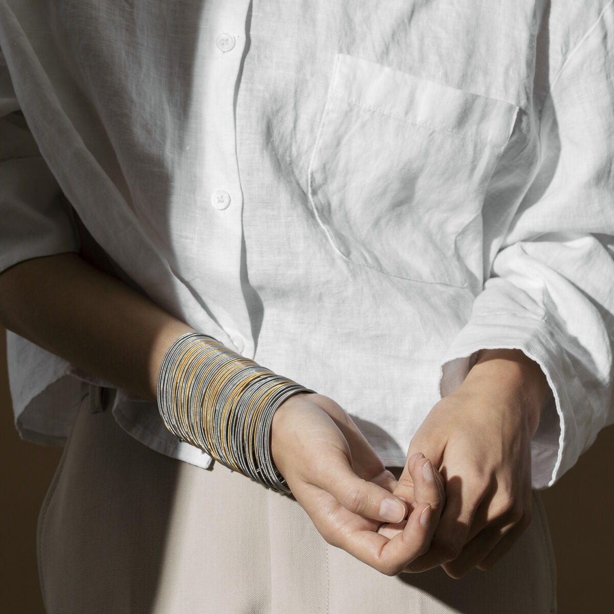Person trägt ein weißes Hemd und beige Hose, dazu ein »Salz und Pfeffer Armband« am Handgelenk. Das Armband hat eine schlichte und elegante Optik in Gold- und Silberfarben.