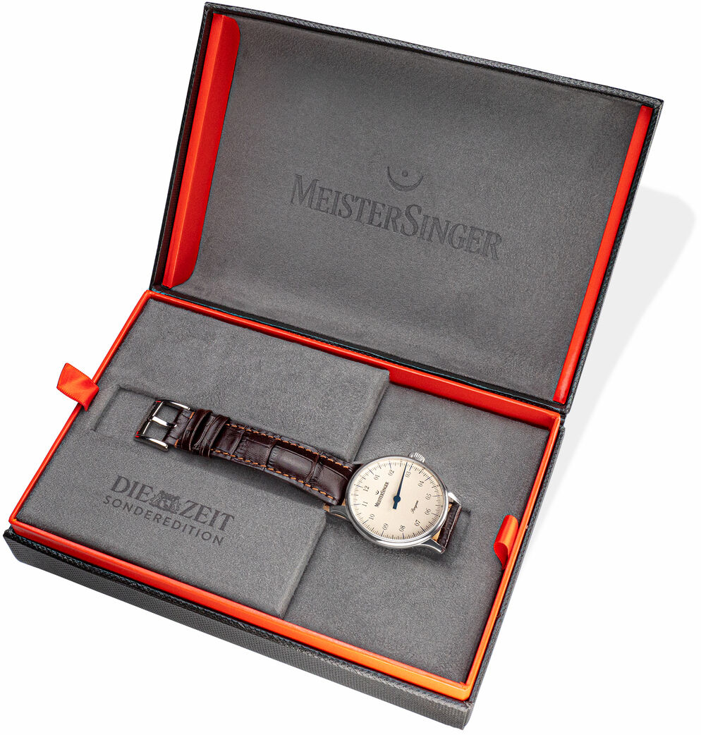 Eine Armbanduhr der Sonderedition »Pangaea« von MeisterSinger, präsentiert in einer eleganten schwarzen Box mit roten Akzenten. Das Uhrgehäuse ist silberfarben und das Armband besteht aus braunem Leder.