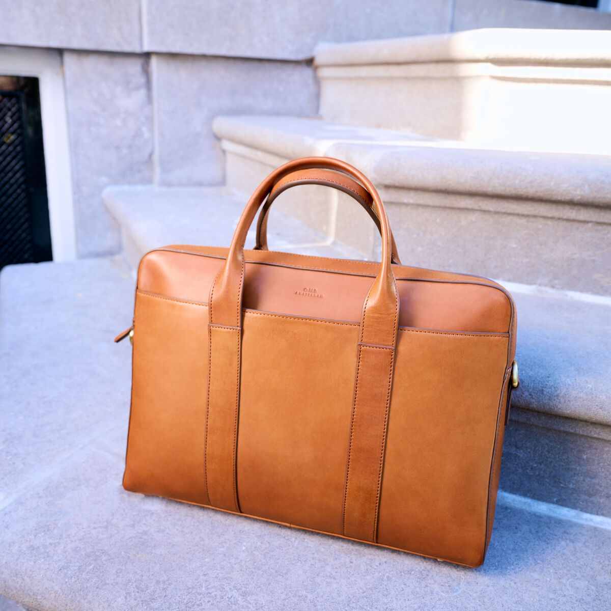 Ledertasche »Harvey« in brauner Farbe, platziert auf einer steinernen Treppe, eleganter und stilvoller Look aus hochwertigem Leder, geeignet für den täglichen Gebrauch, Arbeit oder Reisen.