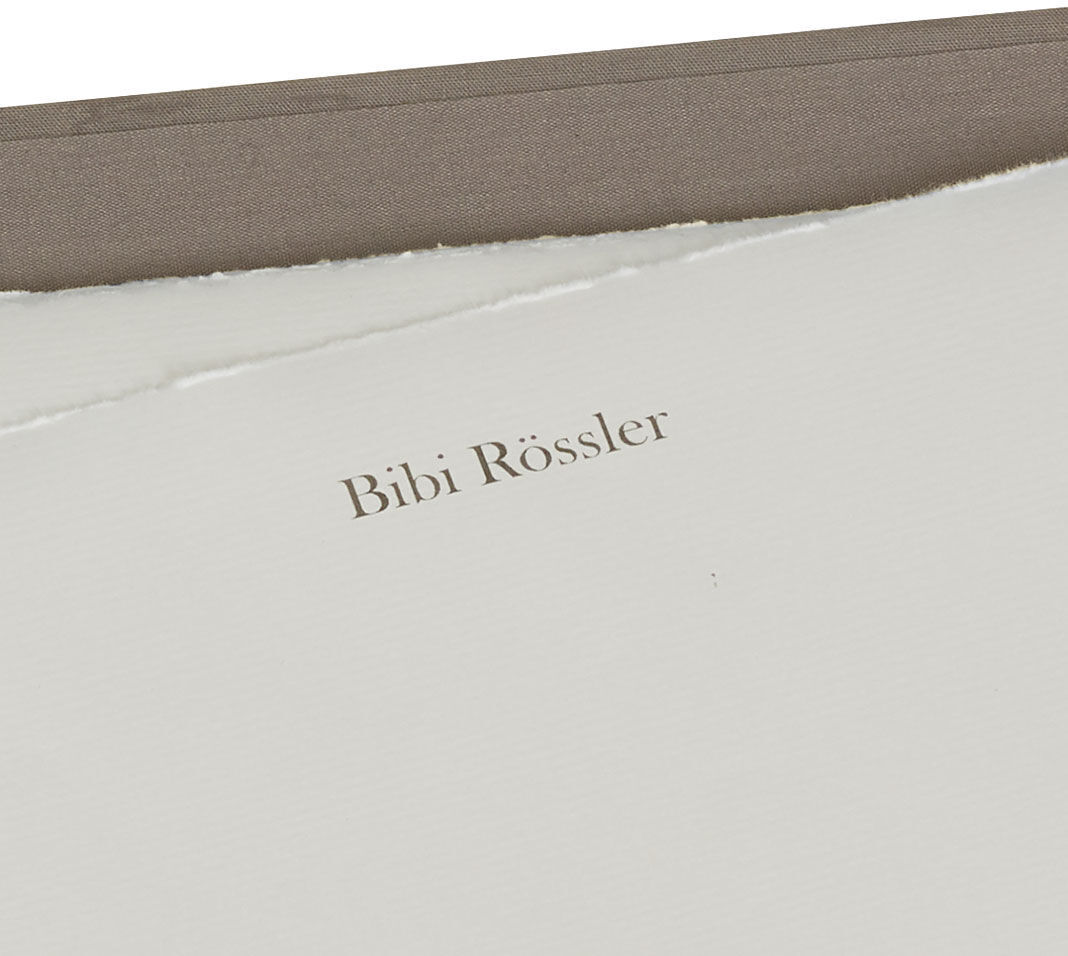 Eine Briefpapiermappe mit hochwertigem Büttenpapier, auf dem der Name 'Bibi Rössler' eingedruckt ist. Die Mappe ist in Weiß- und Beigetönen gehalten und vermittelt eine elegante und exklusive Ausstrahlung.