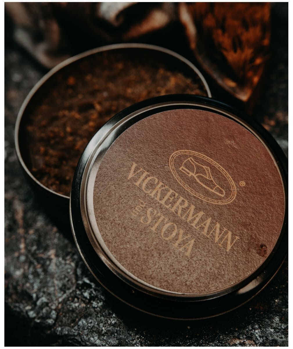 Vickermann und Stoya Lederpflege-Set, bestehend aus zwei runden Behältern, einer davon geöffnet mit brauner Schuhcreme darin, angeordnet auf einer dunklen Oberfläche.