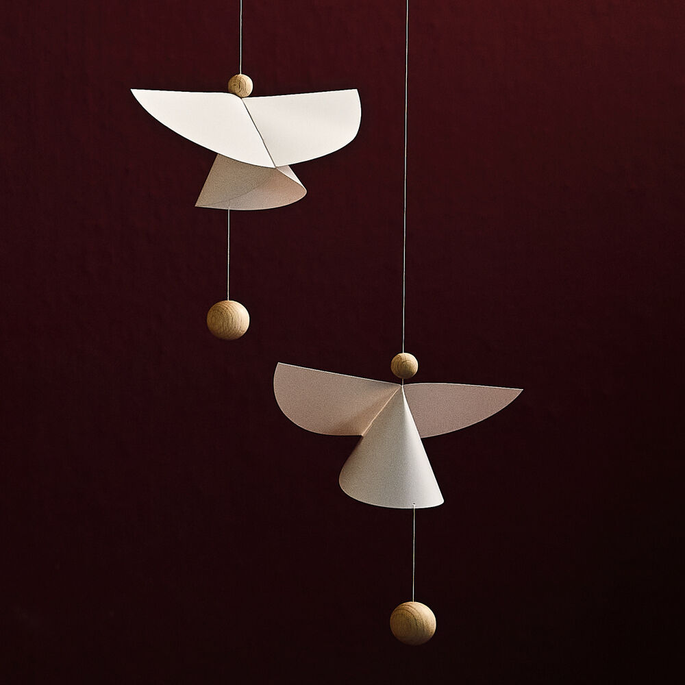 Das Mobile »Schutzengel 5« der Marke Flensted Hanging Art zeigt zwei stilisierte weiße Engel aus Karton mit Naturholzkugeln, schwebend an feinen Fäden vor einem dunkelroten Hintergrund. Das moderne, schlichte Design wirkt ruhig und passt ideal ins Kinderzimmer oder als Weihnachtsdeko.