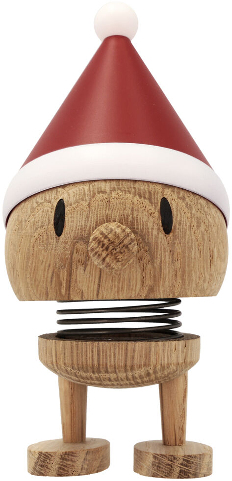 Die Hoptimist Elf Bumble Raw oak von F&H GmbH zeigt eine fröhliche Holzfigur mit runder Form, einer roten Weihnachtsmütze mit weißem Bommel und einer sichtbaren Feder, die den Körper flexibel hält. Die Figur steht auf zwei flachen Füßen und wirkt verspielt.