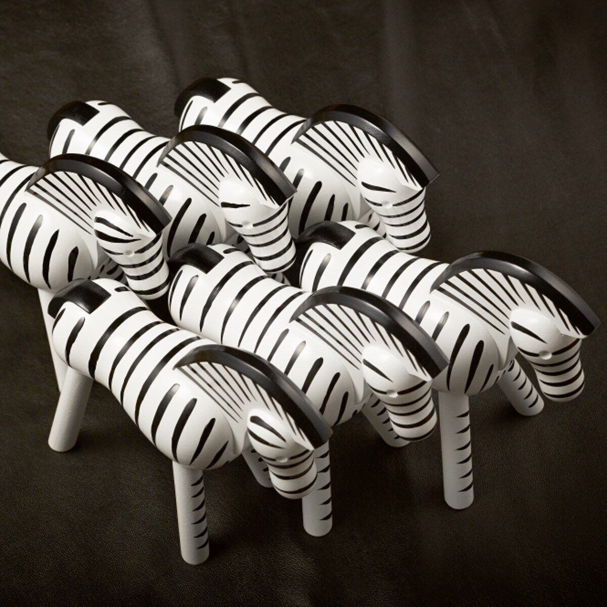 Mehrere Holzfiguren in Form von Zebras, entworfen von Kay Bojesen, auf einer dunklen Oberfläche. Die Figuren sind weiß mit schwarzen Streifen und minimalistischen Designs.
