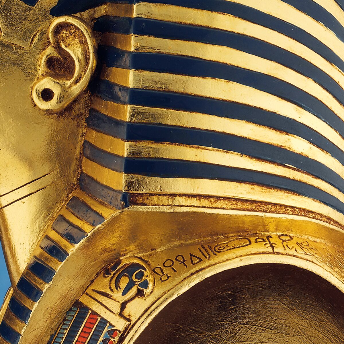 Detailreiche Büste der Goldmaske des Tutanchamun, aus polymerem Kunstguss gefertigt. Frontale Ansicht mit leuchtend goldenem Gesicht, farbigen Schmuckelementen aus Blau, Rot und Weiß sowie schwarzem Streifenmuster auf Kopfbedeckung. Hochwertige, museale Replik auf hellem Untergrund.