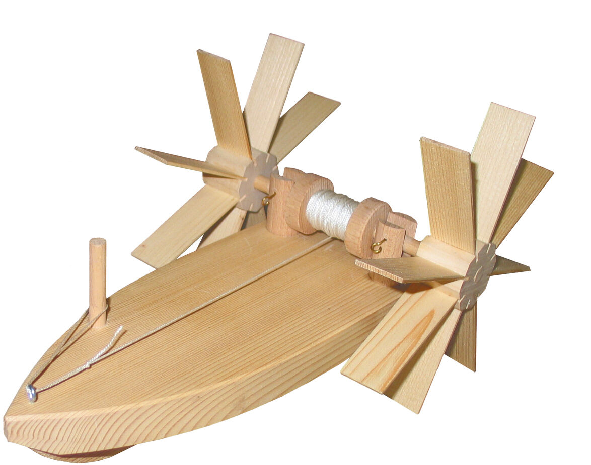 Ein Bausatz „Forelle“ zum Experimentieren, bestehend aus einem Holzboot mit zwei großen Propellern und einer Spule in der Mitte. Verschiedene Teile des Modells sind sichtbar, darunter ein kleinerer Stab an der Vorderseite und eine Schnur, die über die Oberseite des Bootes verläuft.