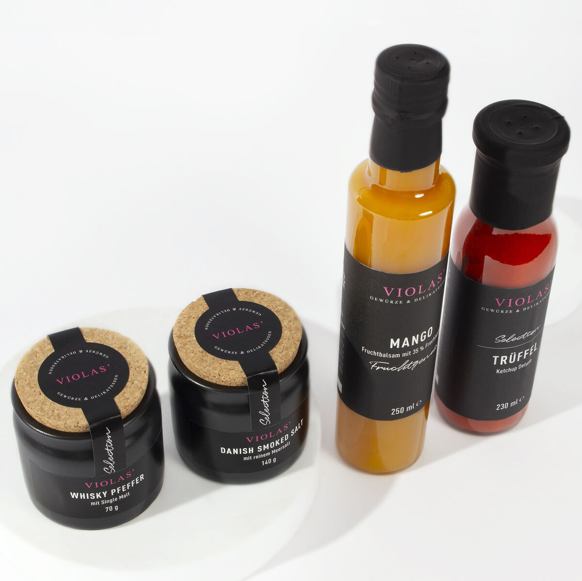 Ein Set von ZEIT Genuss-Selection bestehend aus zwei Gläsern und zwei Flaschen, die verschiedene Gewürze und Soßen enthalten, präsentiert auf einem weißen Hintergrund. Ideal für Feinschmecker und als Geschenkidee geeignet.
