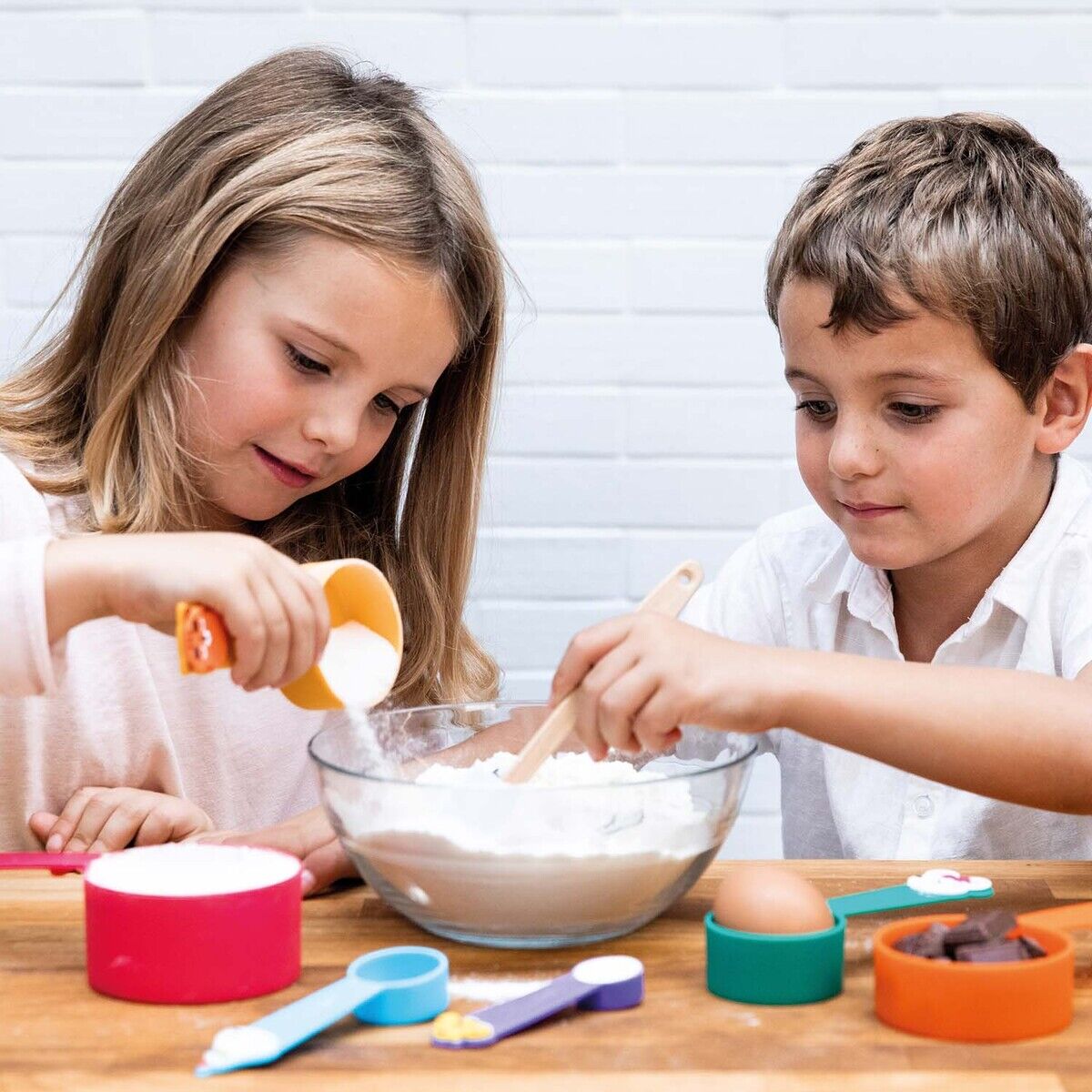 Zwei Kinder backen gemeinsam mit einem Backset von Chefclub, bestehend aus buntem Zubehör und Zutaten wie Mehl und Eiern.