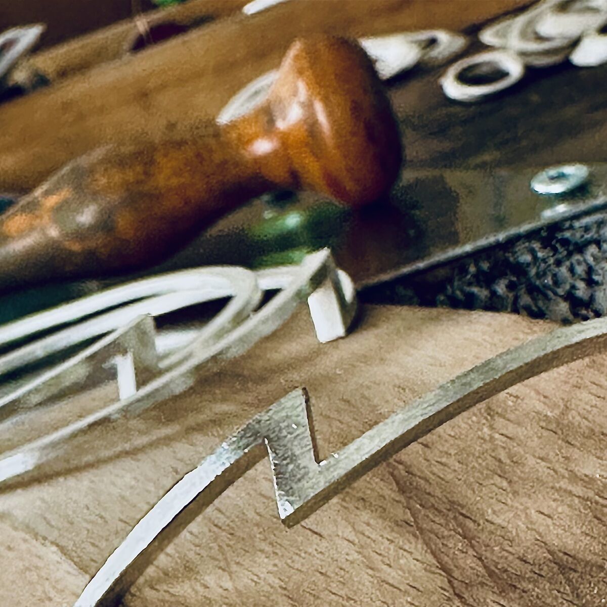 Detailaufnahme einer Werkbank mit einem silberfarbenen ZEIT Sonderedition Armreif »ZEIT« von HML Berlin, feingoldplattiert. Der Armreif liegt neben Werkzeugen wie einer Feile und einem Holzgriff, ringsherum weitere Schmuckelemente und Oberflächen aus Holz und Metall.