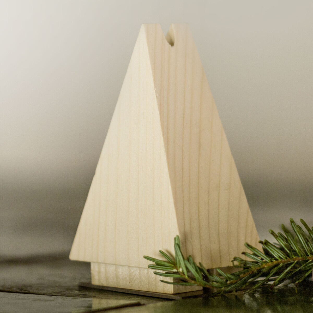 Zwei dreieckige Holzfiguren stehen auf einem Tisch. Eine davon ist geöffnet und die andere geschlossen. Vor den Figuren liegt ein kleiner Zweig Tannengrün.