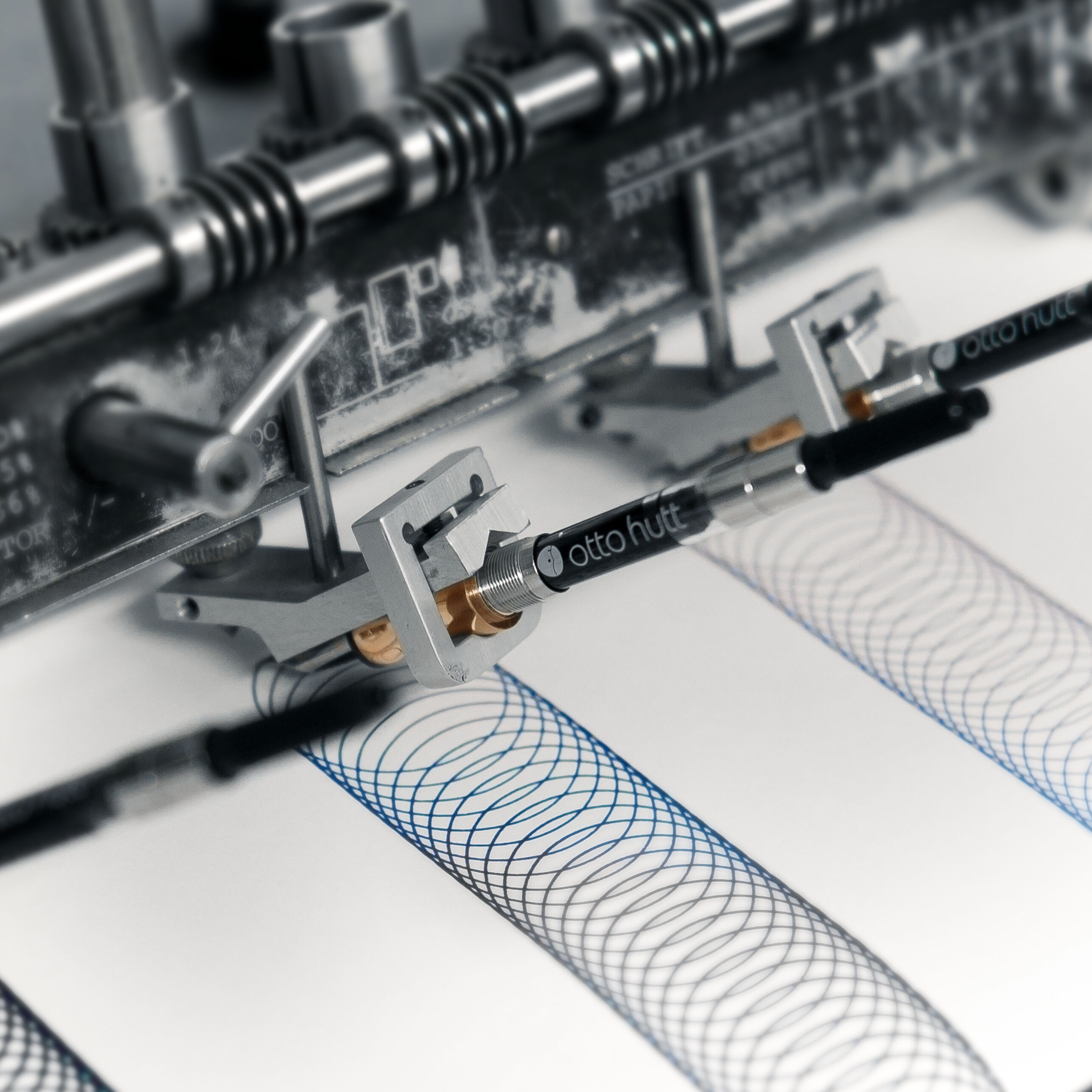 Detailaufnahme eines mechanischen Zeichengeräts mit dem Schriftzug 'otto hutt', das komplexe, sich überlappende Linienmuster auf Papier zeichnet